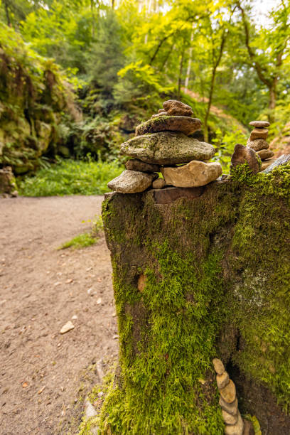 Closeup of cairns or apachitas on a rock formation with moss, dirt trail, trees and green wild vegetation in the background Closeup of cairns or apachitas on a rock formation with moss, dirt trail, trees and green wild vegetation in the background, summer day on the Mullerthal Trail hiking route, Luxembourg luxembourg benelux stock pictures, royalty-free photos & images