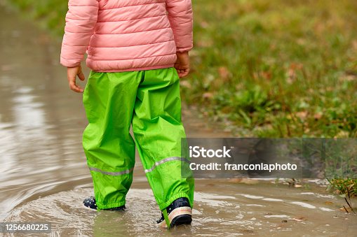 istock Close-up of child girl in waterproof clothing walking through puddle 1256680225