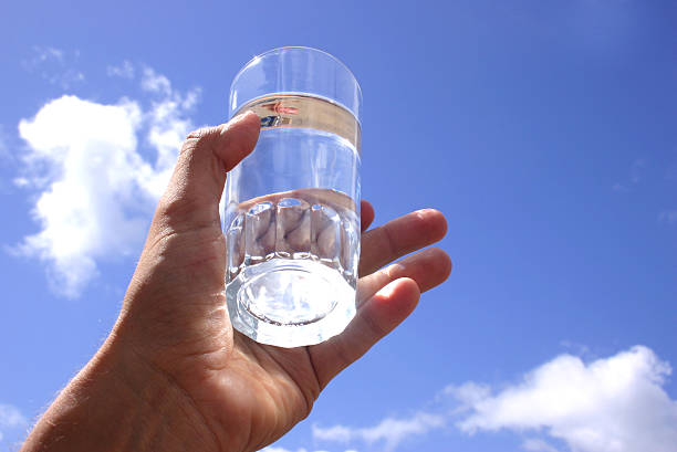 Close-up of clear glass of water held up to a clear sky stock photo