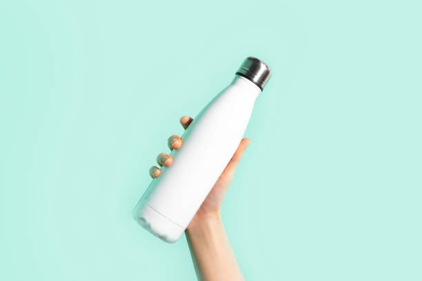 Close-up of female hand, holding white reusable steel stainless eco thermo water bottle with mockup, isolated on background of cyan, aqua menthe color. Be plastic free. Zero waste. Close-up of female hand, holding white reusable steel stainless eco thermo water bottle with mockup, isolated on background of cyan, aqua menthe color. Be plastic free. Zero waste. aqua menthe photos stock pictures, royalty-free photos & images