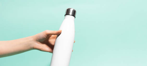Close-up of female hand holding white reusable steel stainless eco thermo water bottle isolated on background of cyan, aqua menthe color. Plastic free. Close-up of female hand holding white reusable steel stainless eco thermo water bottle isolated on background of cyan, aqua menthe color. Plastic free. aqua menthe photos stock pictures, royalty-free photos & images