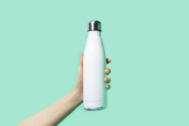 Close-up of female hand, holding white reusable steel stainless eco thermo water bottle on background of cyan, aqua menthe color. Be plastic free. Zero waste. Close-up of female hand, holding white reusable steel stainless eco thermo water bottle on background of cyan, aqua menthe color. Be plastic free. Zero waste. aqua menthe photos stock pictures, royalty-free photos & images