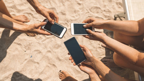 close-up van vrouwelijke handen die telefoons houden die op sociaal netwerk babbelen of online op het strand winkelen. dwangmatig smartphone- en internetgebruik (verslaving) van jongeren (millennials) concept - beach game group stockfoto's en -beelden