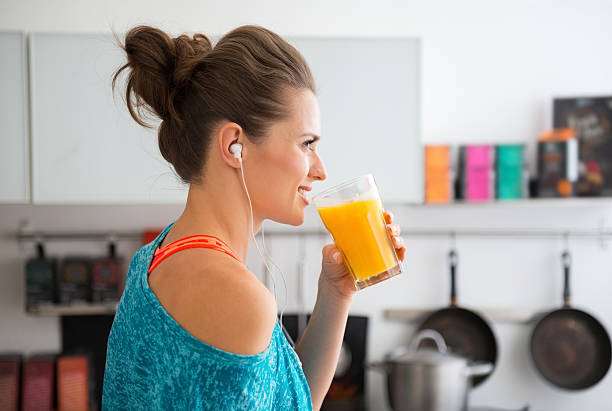 Closeup of fit woman in profile starting to drink smoothie In her modern kitchen, a woman in profile is about to drink her freshly-made smoothie, which is packed with vitamins. A healthy lifestyle is so much fun. juice drink stock pictures, royalty-free photos & images
