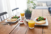 Close-up of breakfast served on wooden table. Fresh meal are in containers at home. Potted plant is by food and drink.