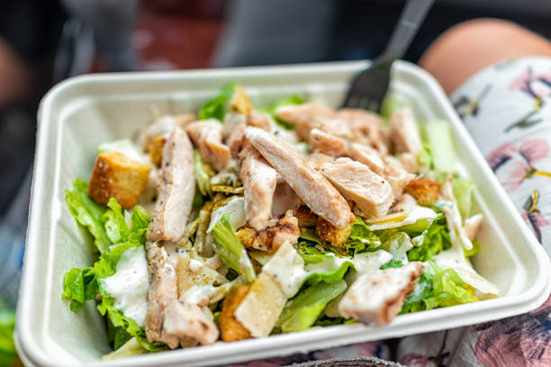 Closeup of fresh creamy caesar dressing salad with chopped vegetables romaine lettuce greens and grilled chickens strips in tray carton as quick fast lunch in car on road trip stock photo