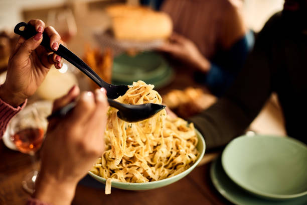 close-up of friends eating pasta for dinner at dining room table. - eten stockfoto's en -beelden