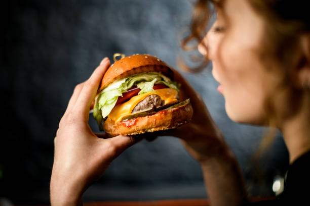 Close-up of hamburger in hands of young woman. Close-up of big tasty burger sandwich in hands of young woman. Time for little snack biting photos stock pictures, royalty-free photos & images