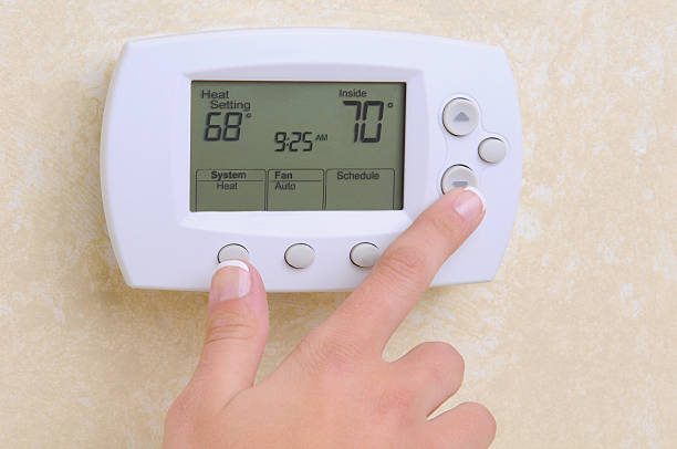 Closeup of Hand and Thermostat Closeup of a womans hand setting the room temperature on a modern programable thermostat. thermostat stock pictures, royalty-free photos & images