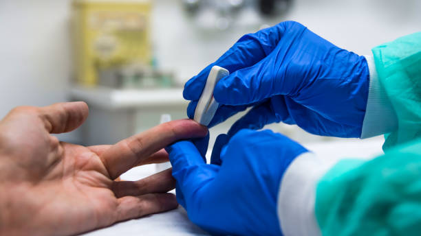 primo piano delle mani di un infermiere con attrezzature di protezione individuali e paziente, nel processo di raccolta del sangue per fare un rapido test per covid-19(coronavirus), in un reparto ospedaliero con elementi sanitari sullo sfondo. - cuadrado foto e immagini stock