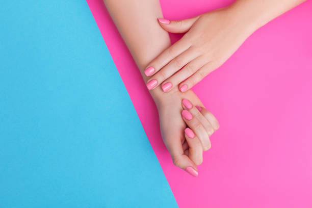 Closeup of hands of a young woman with manicure on nails against pink background stock photo