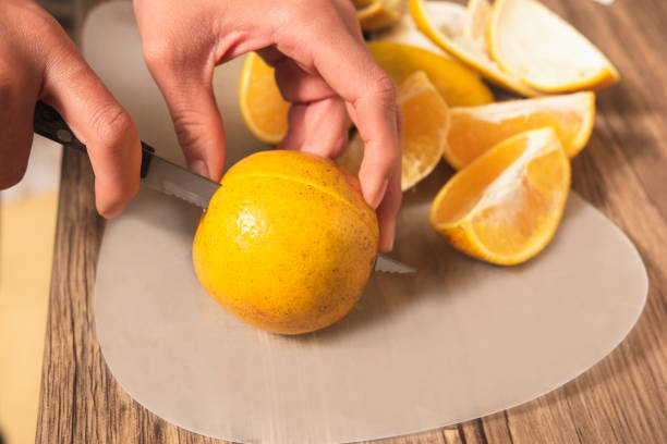 closeup of latin girl's hand cutting an orange fruit into slices stock photo