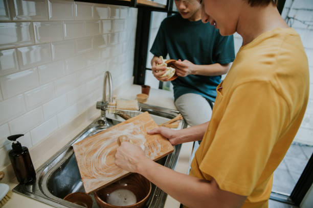 Close-up of LGBTQIA people cleaning
cutting board with eco dish brush beside his friend at home-stock photo stock photo