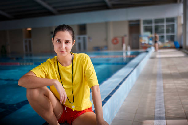 Close-up of lifeguard smiling looking sitting on indoor pool side stock photo