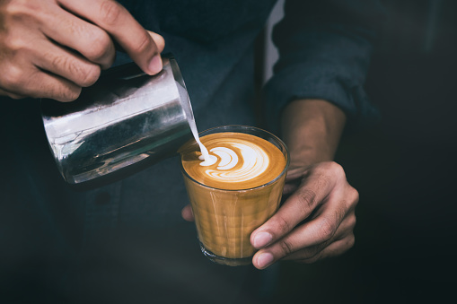 Close-up of male barista hand holding and pouring hot milk for prepare latte art on piccolo latte cup of coffee.