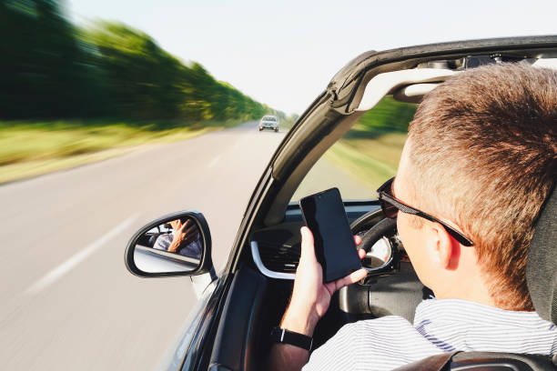 자동차를 운전하는 동안 스마트 폰을 사용하는 남자의 클로즈업. 다가오는 트래픽으로 운전. 위험한 움직임. 전화로 산만. 남자는 운전하는 동안 전화로 메시지를 씁니다. 효과 흐린 모션 - 부주의한 뉴스 사진 이미지