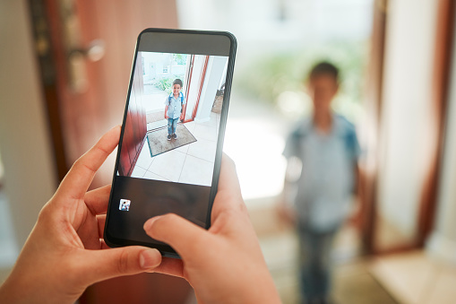 Closeup of mother taking photo of son on first day of school.   Hands taking picture on cellphone of kindergarten boy standing by the door and ready to leave home. Proud mom documenting childhood