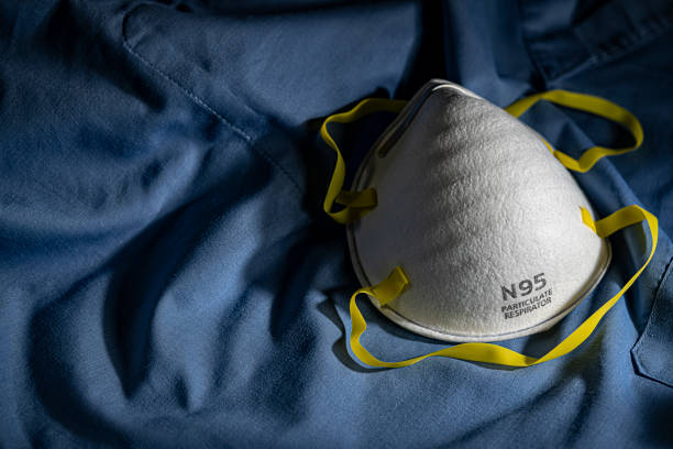 Closeup of N95 Mask on Blue Scrubs N95 PPE protective mask resting on blue medical scrubs with copy space n95 mask stock pictures, royalty-free photos & images