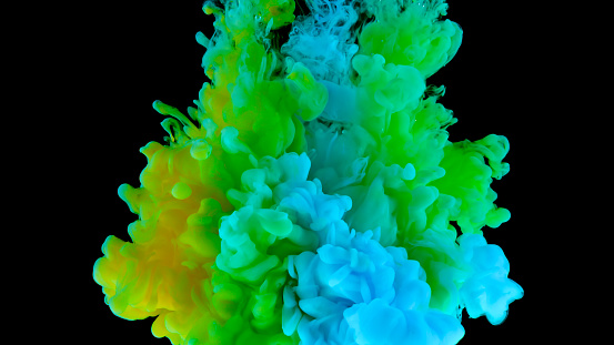 Close-up of green, blue and yellow colored paint dissolving in water against black background.
