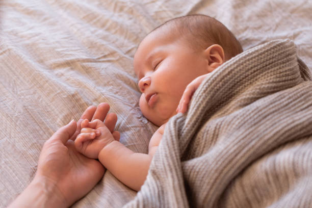 寝ているベッドの上の母の手で赤ちゃんの手のクローズ アップ。新しい家族と赤ちゃん睡眠の概念 - 赤ちゃん　寝る ストックフォトと画像
