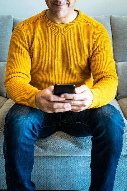 Close-up of smiling man using smartphone sitting on sofa stock photo