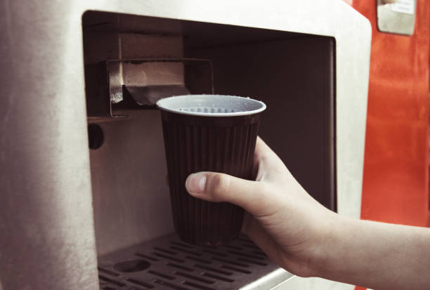 nahaufnahme der hand nimmt ein glas wasser aus dem gerät mit wasser. getönten - kaffeeautomat stock-fotos und bilder
