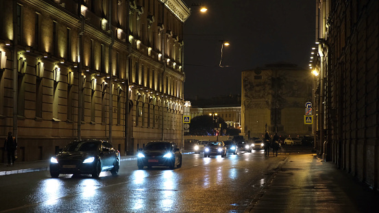 Close-up of the Saint Petersburg's street with moving cars at night and two horses with riders walking along the road. Urban night scenery