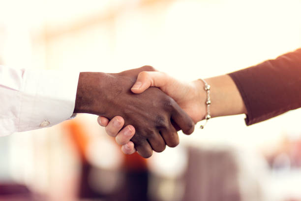 closeup of white and black shaking hands over a deal - handshake imagens e fotografias de stock