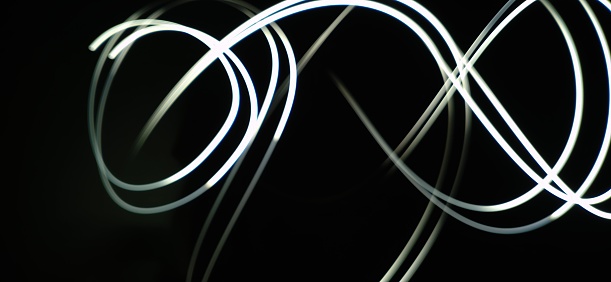 Closeup of White neon Curved Wave pattern abstract flowing in a isolated black background with copy space made using  photography technique called Long exposure.