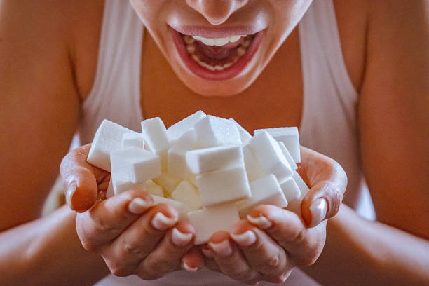 Close-up of woman holding a hands full of sugar cubes in front of her open mouth stock photo
