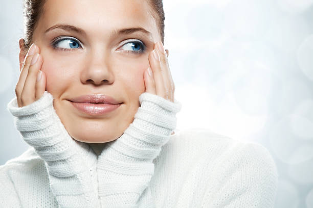 Close-up of woman with hands on her face in white sweater stock photo