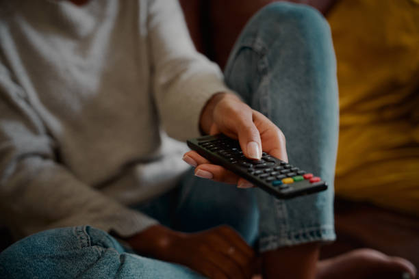 Closeup of young female hand holding remote control and changing channel at home watching television alone Woman hand holding television remote at home remote control stock pictures, royalty-free photos & images