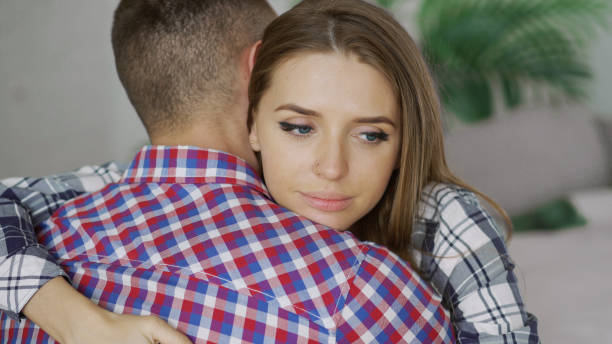 Closeup of young upset couple embrace each other after quarrel. Woman looking wistful and sad hug her boyfrined at home stock photo