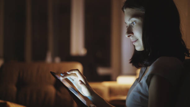 Close-up of young woman surfing tablet computer at night at home stock photo