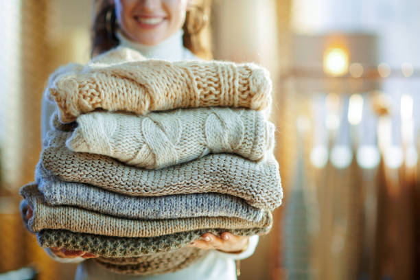 Closeup on happy elegant housewife holding pile of sweaters stock photo