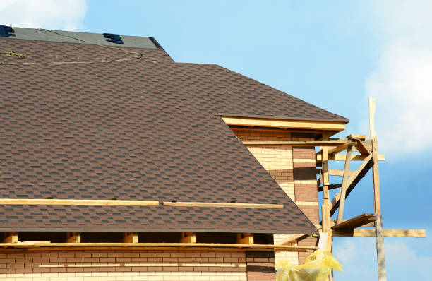 Een close-up op onvoltooide dakbouw, die met dimensionale dakshingles van het asfalt, en bakstenen muren van het huis met steigers tegen blauwe hemel wordt behandeld.​​​ foto