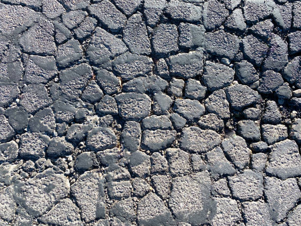 closeup overhead view of cracked asphalt road street damaged in sunlight decay drought stock photo