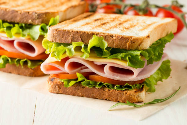 close-up photo of a club sandwich. sandwich with meat, prosciutto, salami, salad, vegetables, lettuce, tomato, onion and mustard on a fresh sliced rye bread on wooden background. olives background. - sandwich imagens e fotografias de stock