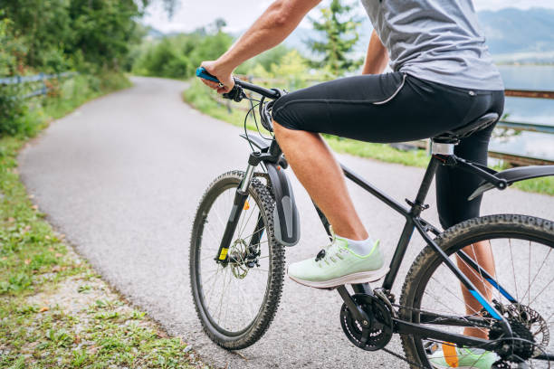 Close-up photo of a man dressed in cycling clothes starting riding a modern bicycle on the asphalt out-of-town bicycle path. Active sporty people concept image. stock photo