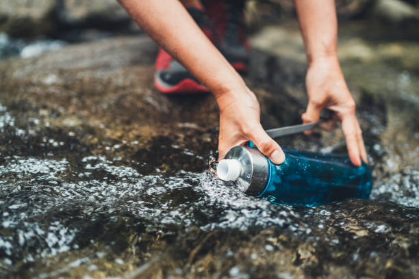 Close-up photo of female hands filling up a fresh cold mountain stream water into the plastic touristic bottle while water break on the tourist hiking route. Active people or water resources concept. stock photo