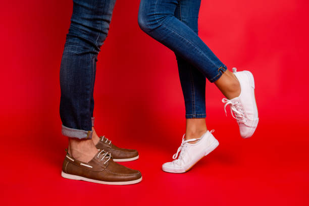 Closeup photo of woman and man legs in jeans, pants and shoes, girl with raised leg, stylish couple kissing during date, isolated over red background, he vs she Closeup photo of woman and man legs in jeans, pants and shoes, girl with raised leg, stylish couple kissing during date, isolated over red background, he vs she many shoe male stock pictures, royalty-free photos & images