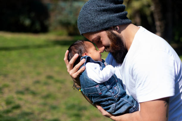 Close-up portrait of happy young father hugging and kissing his sweet adorable newborn child. stock photo