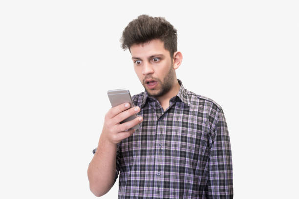 Close-up portrait of shocked young man looking at smart phone's screen receiving bad news on a white background stock photo