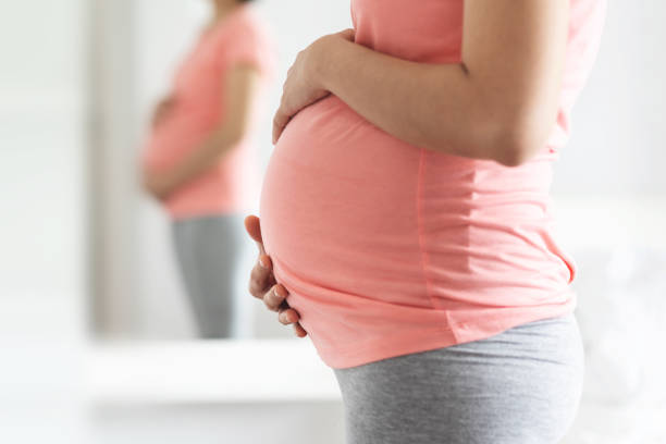 Close-Up Pregnant Woman in pink shirt standing touching her belly with copy space. stock photo