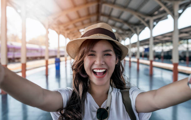 Close-up selfie-portrait of attractive girl with long hair standing at railway statioin Close-up selfie-portrait of attractive girl with long hair standing at railway station. She is smiling to the camera and shows cool look. Straw hat on head. On holiday and vacation. railroad station photos stock pictures, royalty-free photos & images