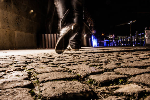 Closeup shot of a man walking on the stone ground in the street at night stock photo