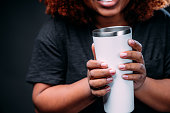istock Close-Up Shot of a Young African American Woman Holding a Generic Plain White Stainless Steel Coffee Mug in front of a Dark Background 1299197832