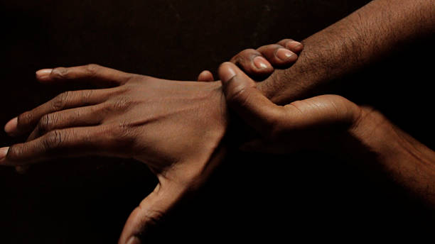 close-up shot of an African American man holding his wrist in black background stock photo