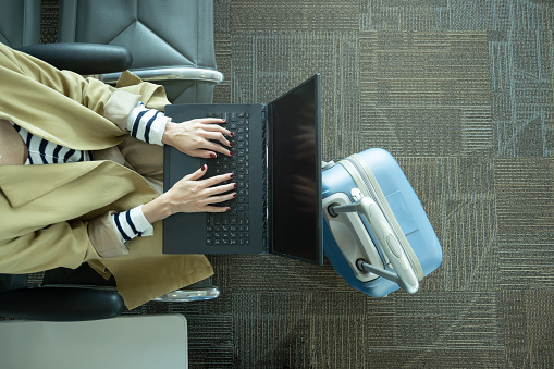 Top view of unrecognizable woman working with laptop in airport next to luggage with copy space
