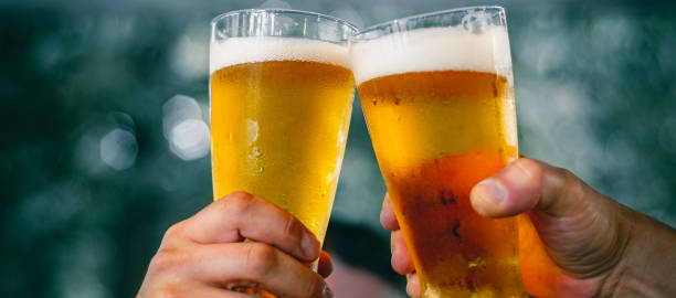 close-up view of a two glass of beer in hand. beer glasses clinking at outdoor bar or pub - beer imagens e fotografias de stock